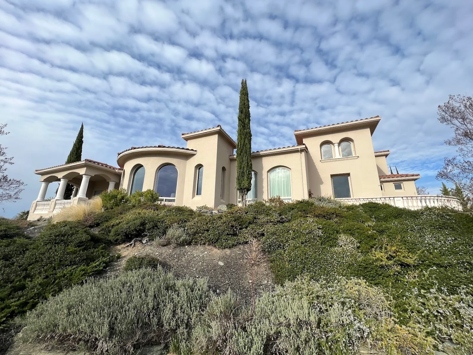 Cream stucco Mediterranean home with arched windows and painted exterior trim on hillside