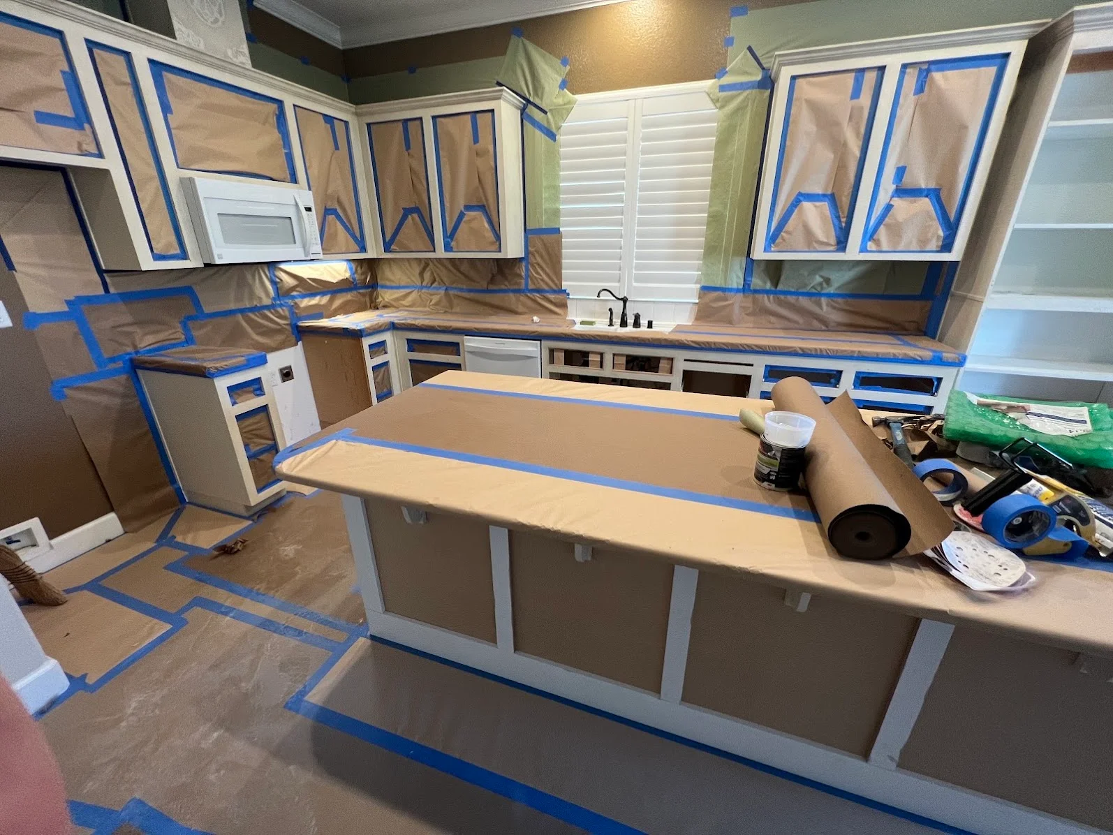 Kitchen cabinets masked with blue tape and kraft paper during painting preparation and refinishing