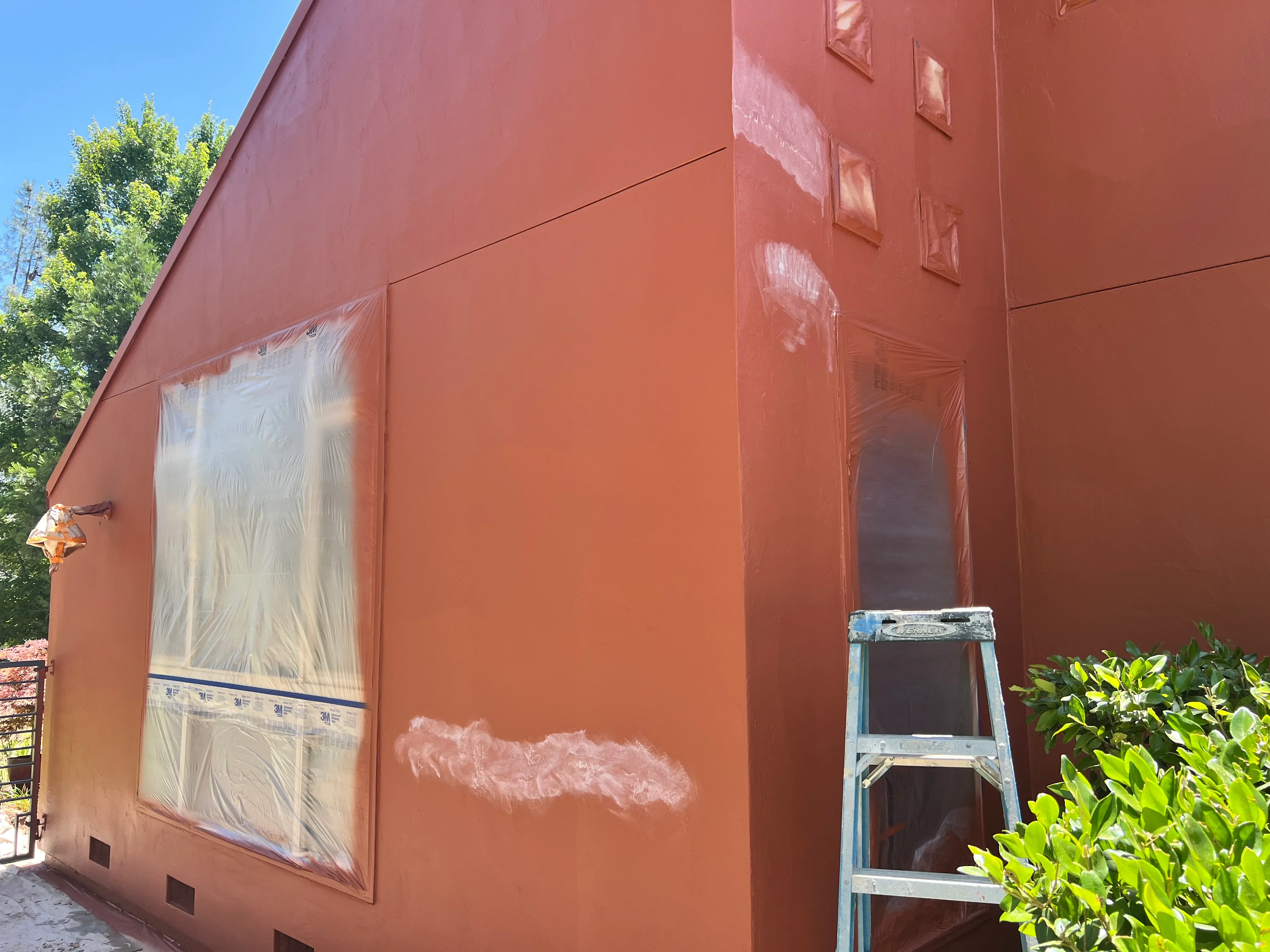 Terracotta-painted house exterior with protected windows and ladder setup during painting project