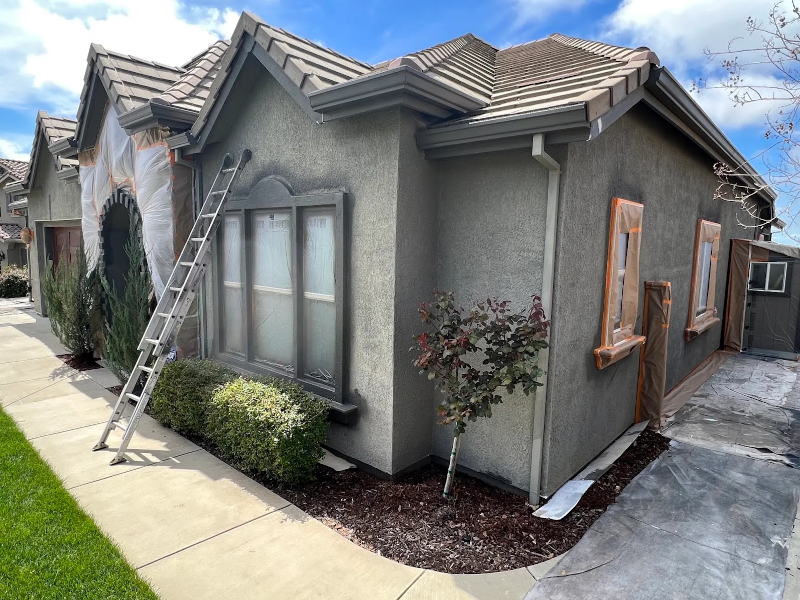 Stucco house exterior with fresh gray paint, metal roof, and protective coverings during painting project