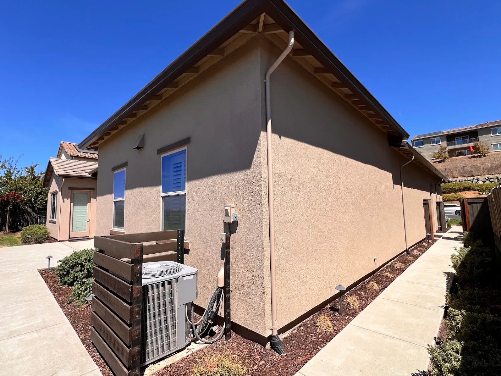 Exterior stucco wall painted beige with blue window trim and metal downspout