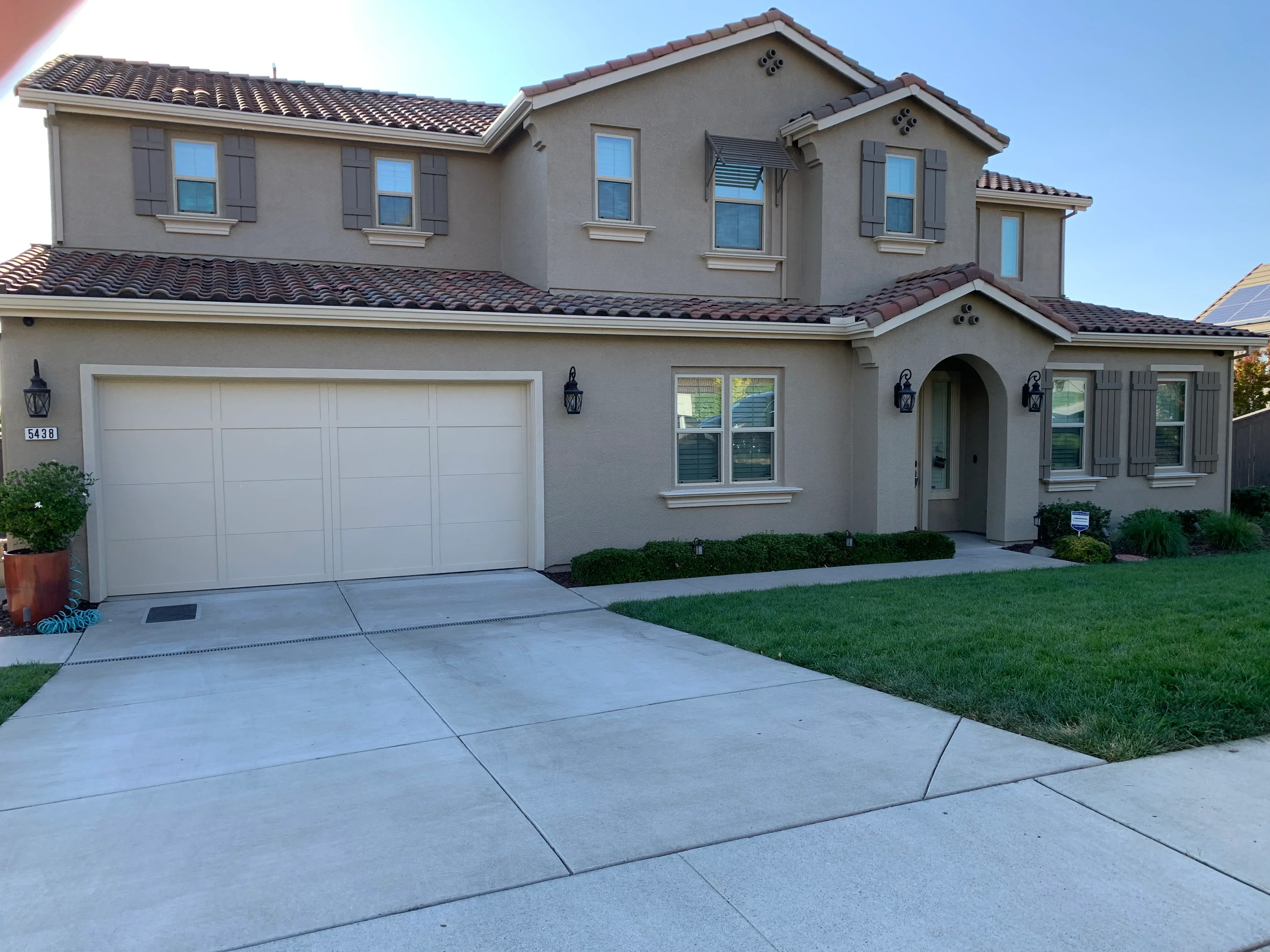 Two-story taupe stucco house with white trim, clay tile roof, and white garage door