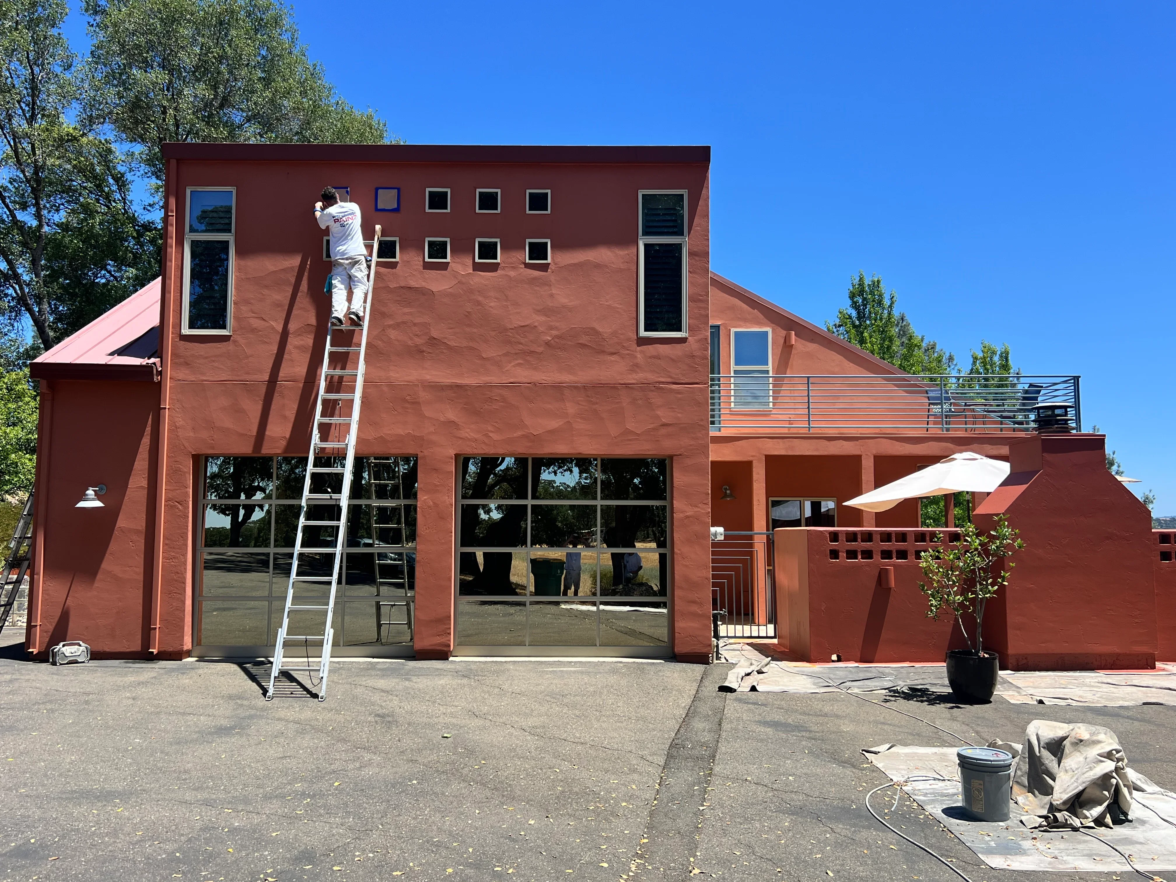 Painter on ladder applying red exterior paint to modern commercial building facade