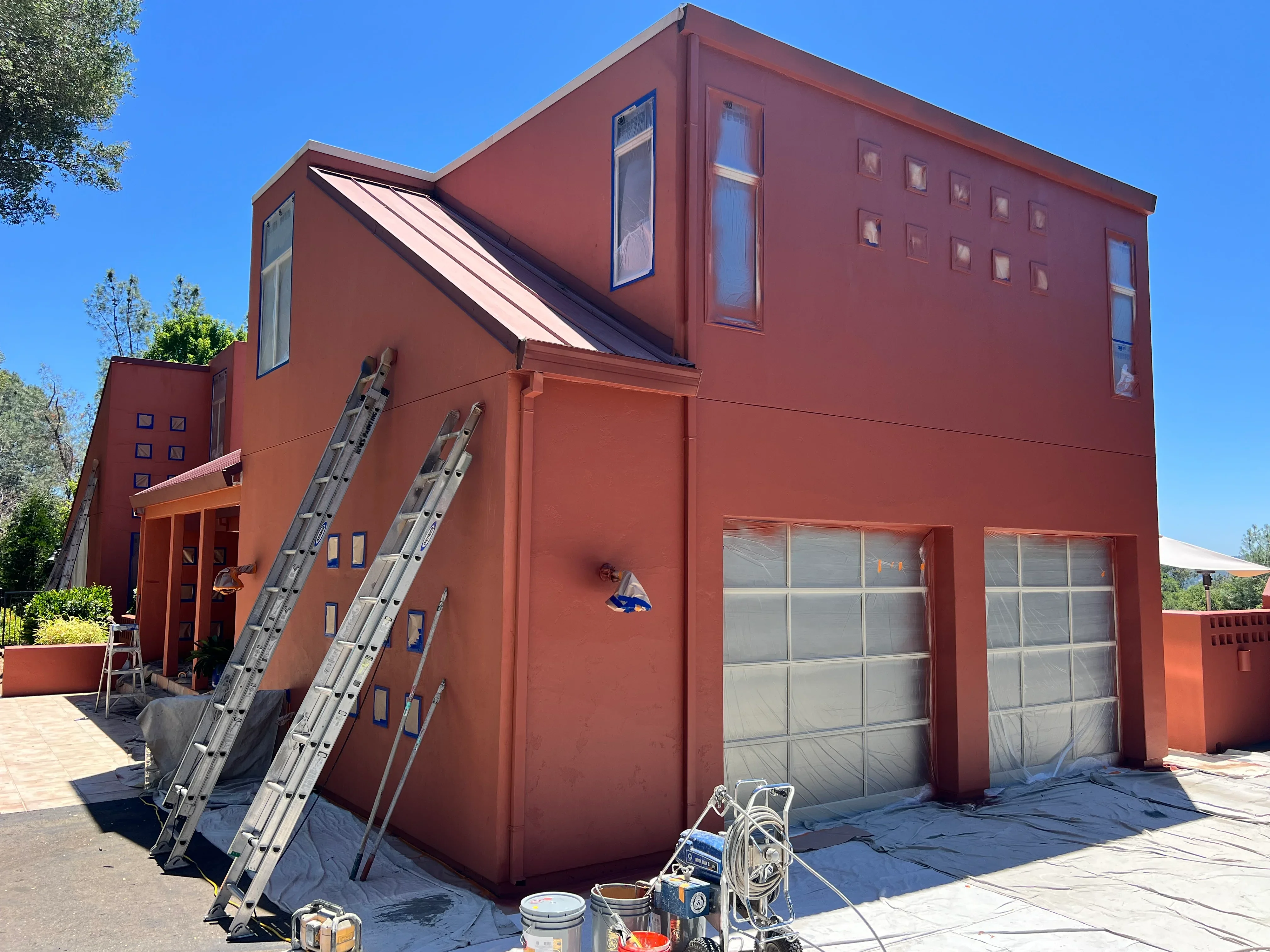 Rust-red painted commercial building with gray garage doors and ladder setup for exterior painting work