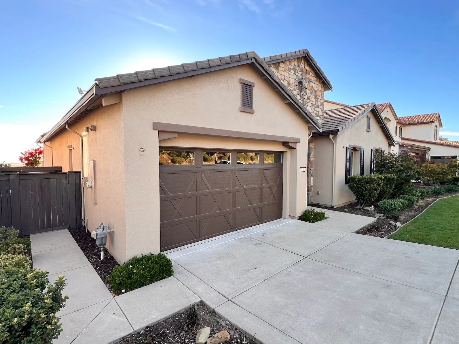 Tan stucco house with brown garage door, stone gable, and freshly painted exterior trim