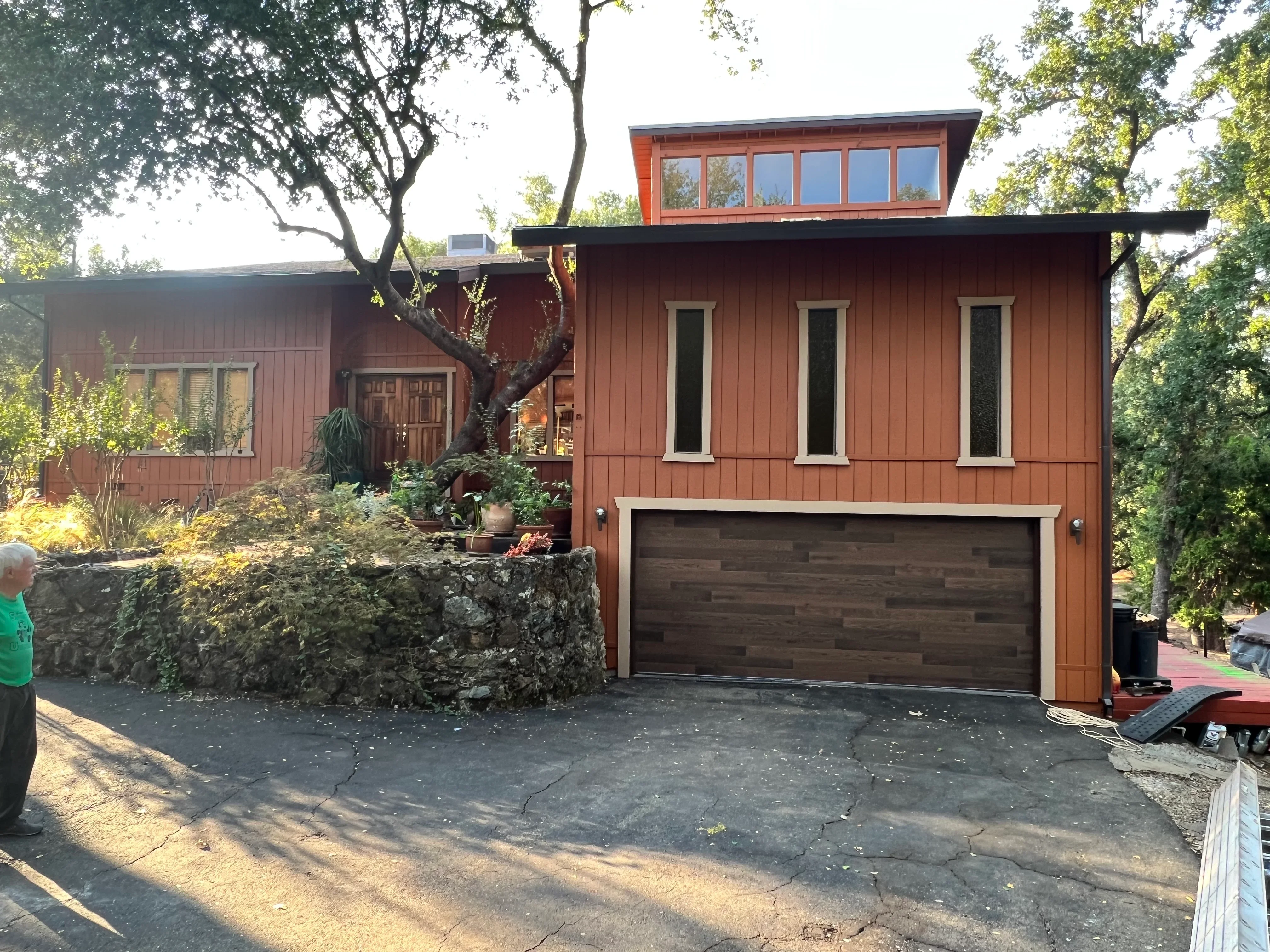 Modern rust-red home with painted vertical siding, dark garage door, and white-trimmed windows