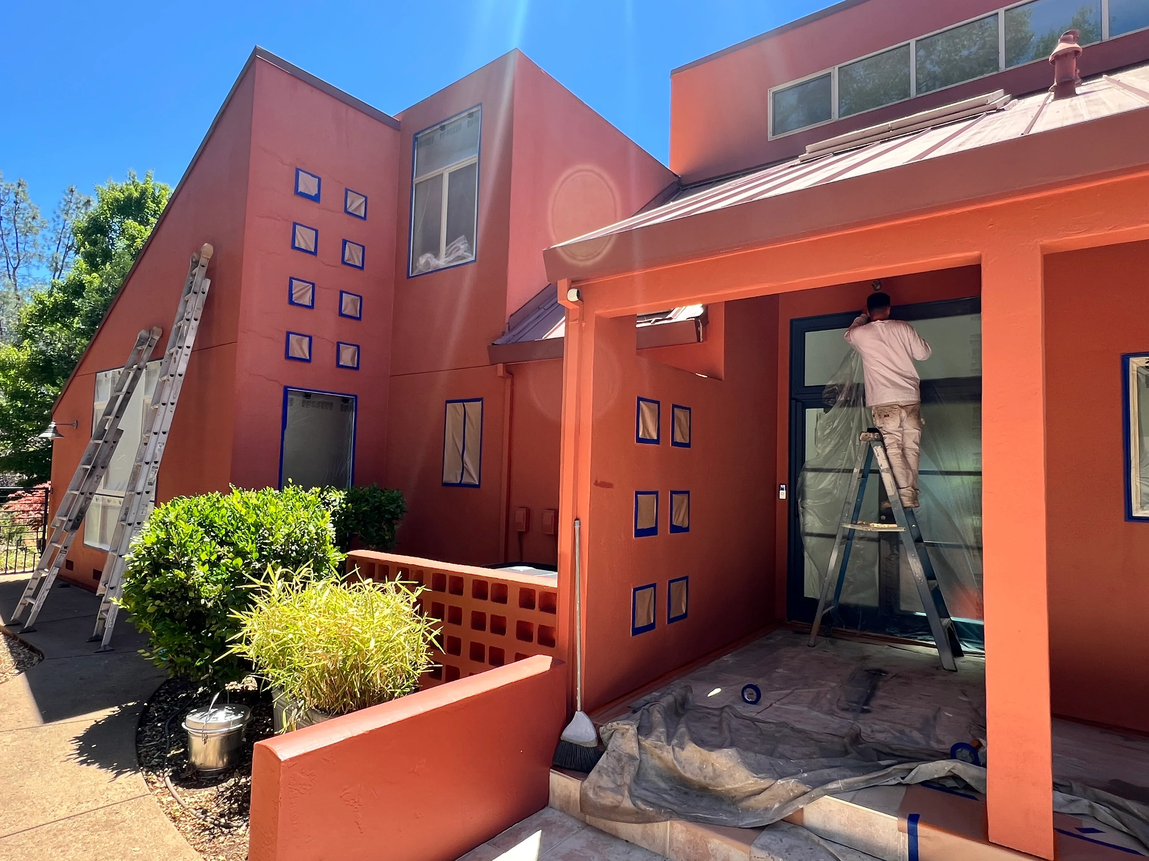 Rust-orange and red painted modern home exterior with worker on ladder during painting project