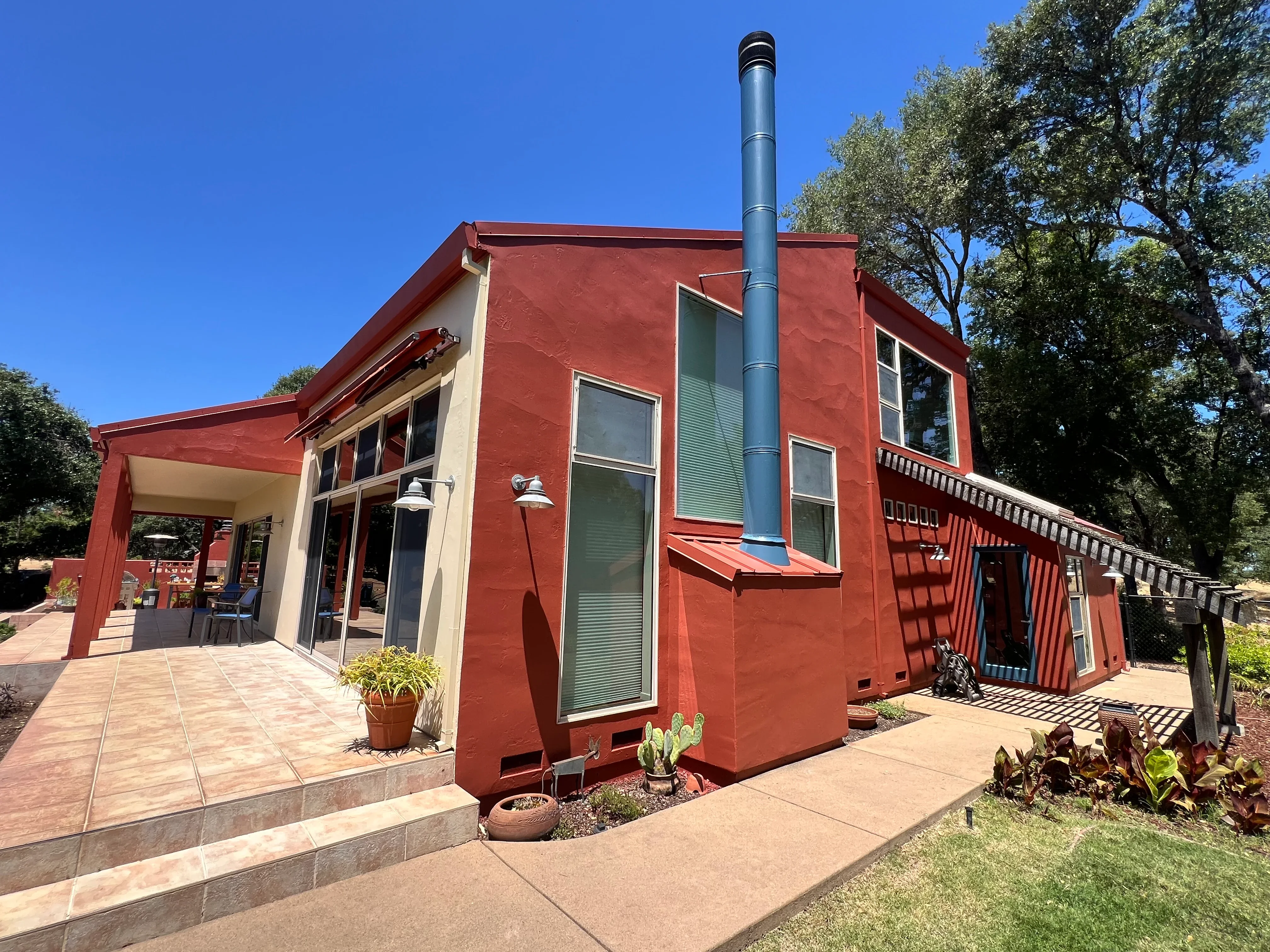 Red stucco house with cream trim, metal chimney, and landscaped front yard