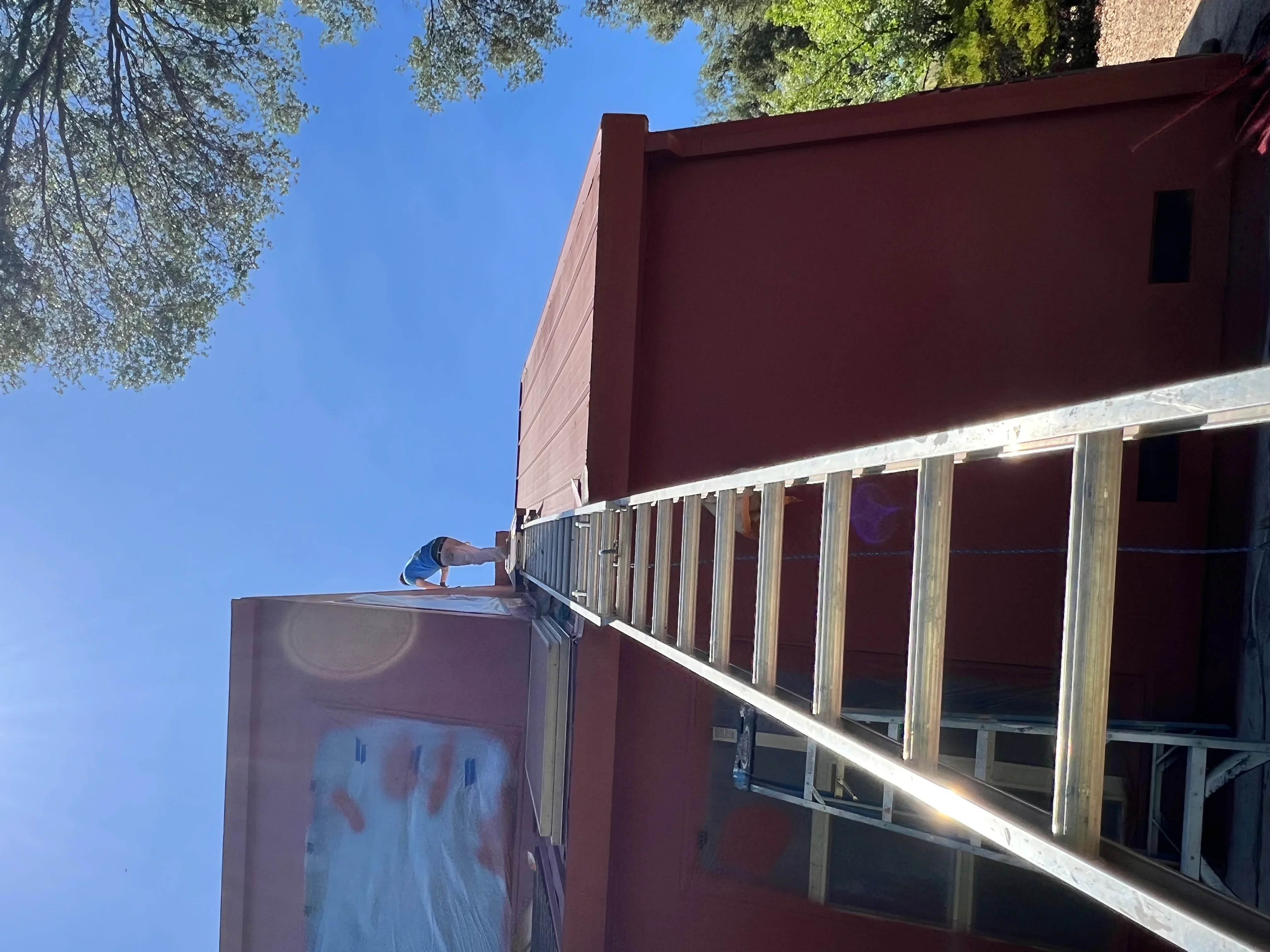 Worker painting large burgundy exterior wall of commercial building with aluminum window frames