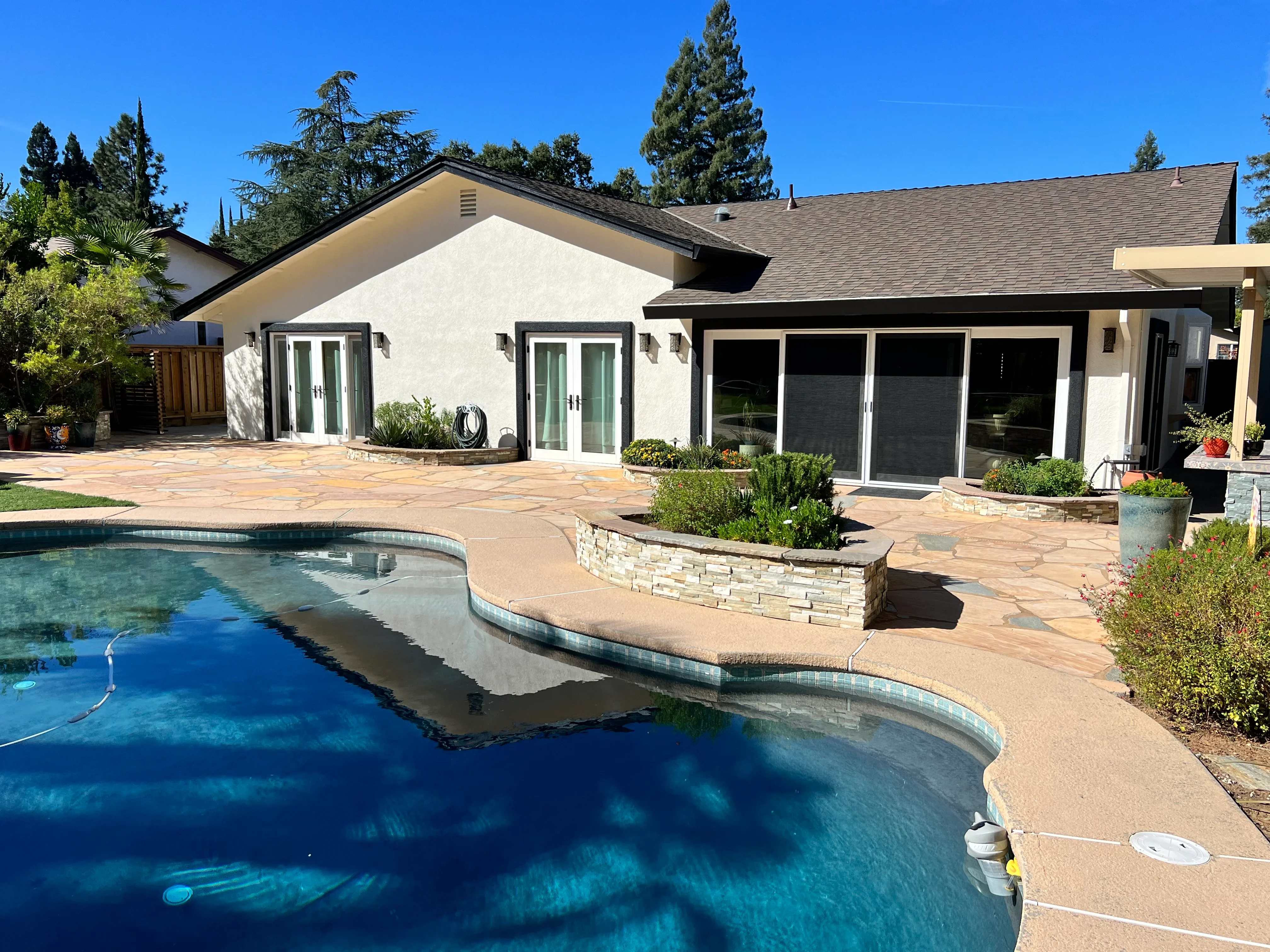 White stucco home with dark trim, pool deck, and updated exterior paint finish