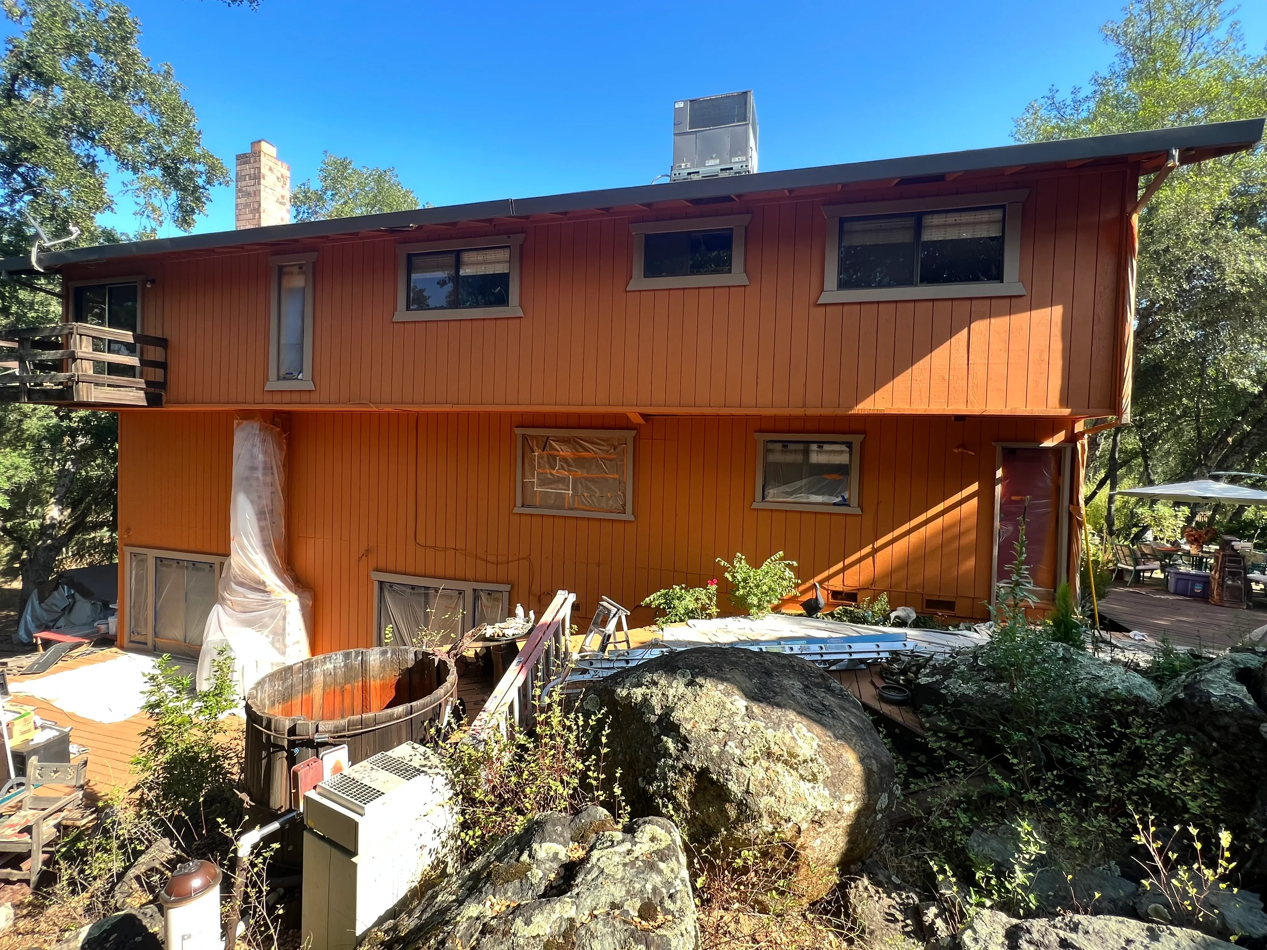 Two-story rust-orange painted home with vertical siding, multiple windows, and brick chimney