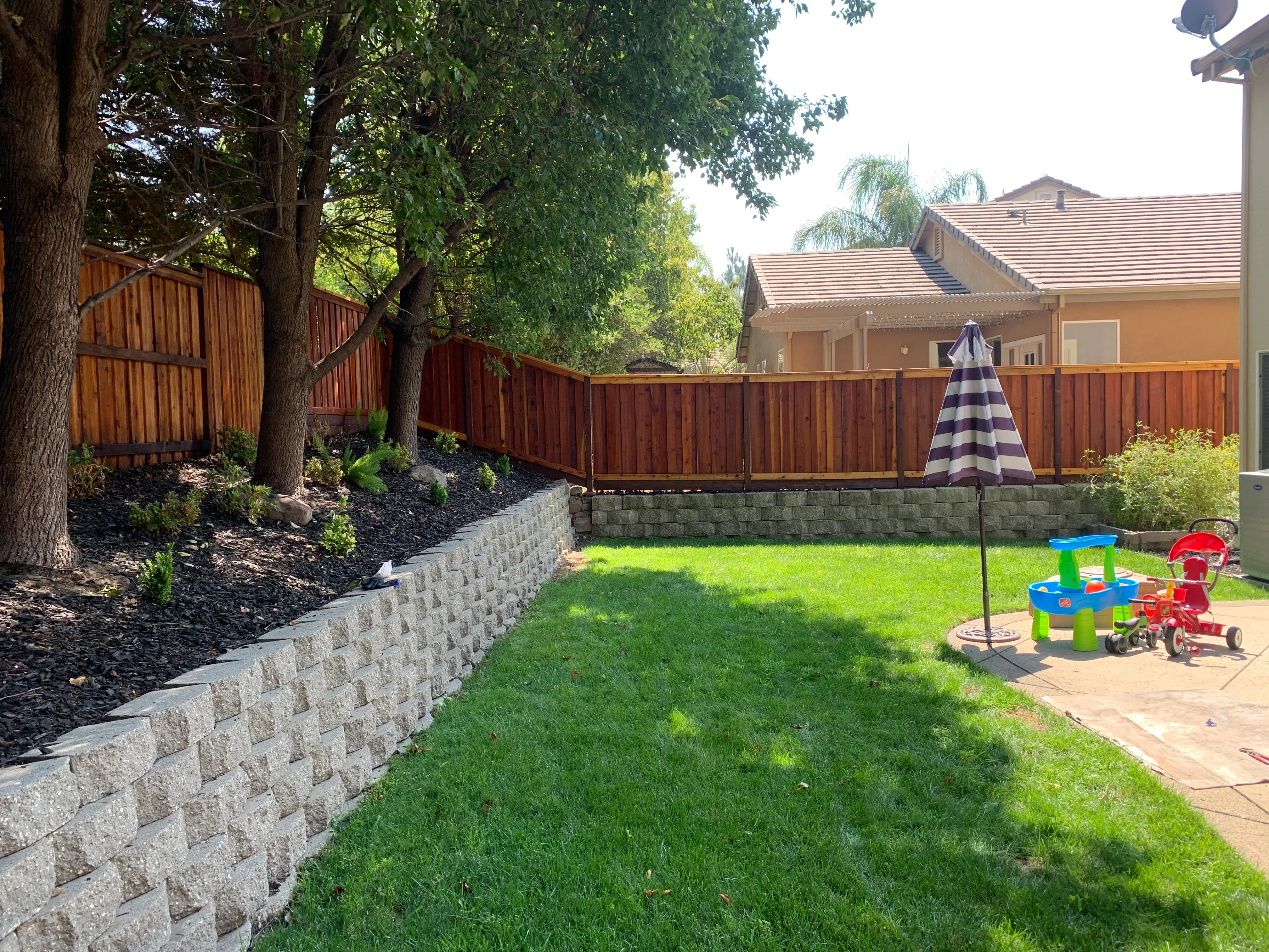 Stained wooden privacy fence surrounding residential backyard with retaining wall and lawn
