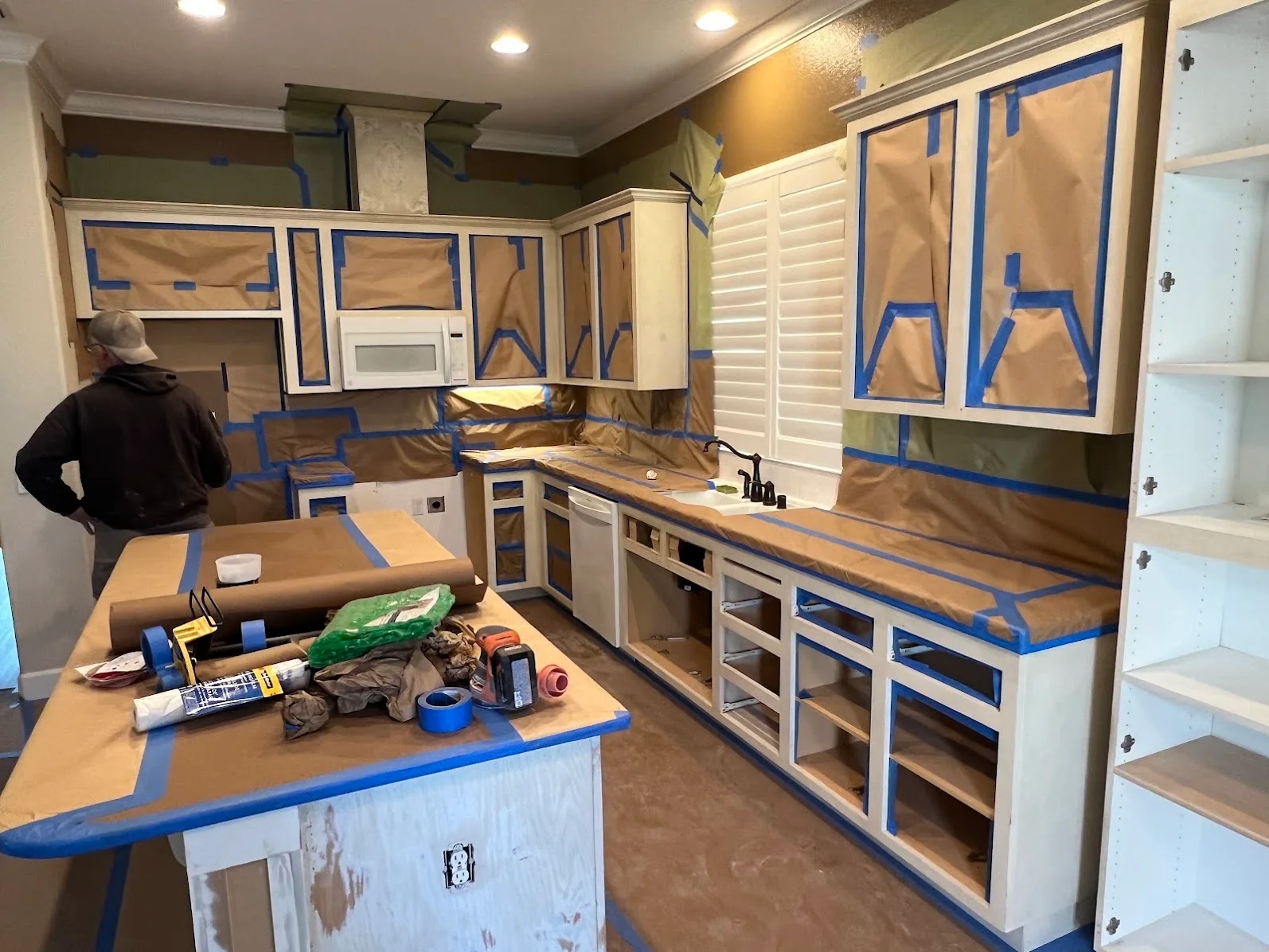 Kitchen interior with blue painter's tape masking cabinets, counters, and appliances during painting prep