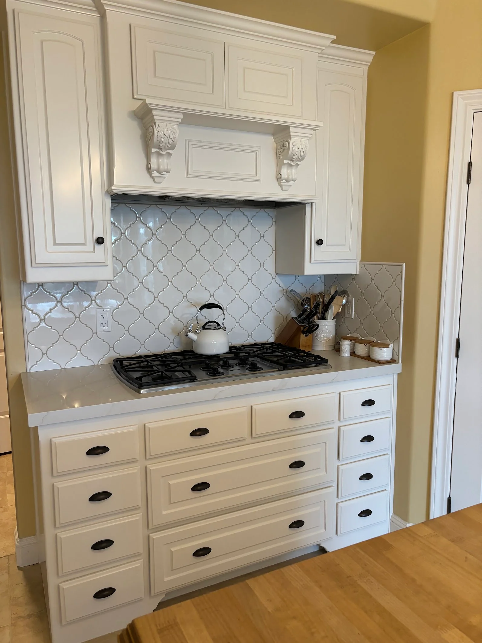 White painted kitchen cabinets with raised panels, decorative corbels, and painted crown molding above gas cooktop