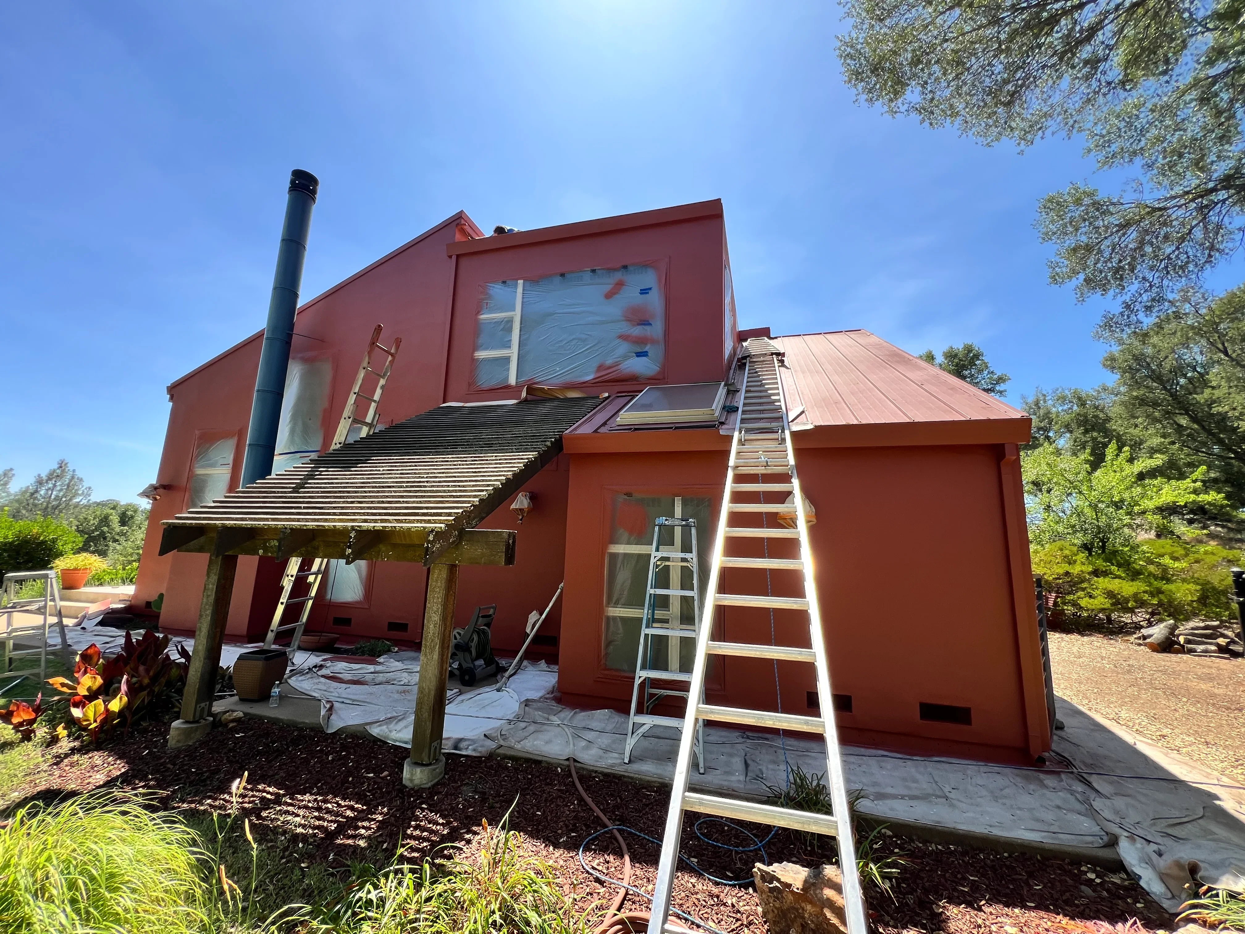Red modern home exterior with fresh paint, metal roof, and white trim during painting project