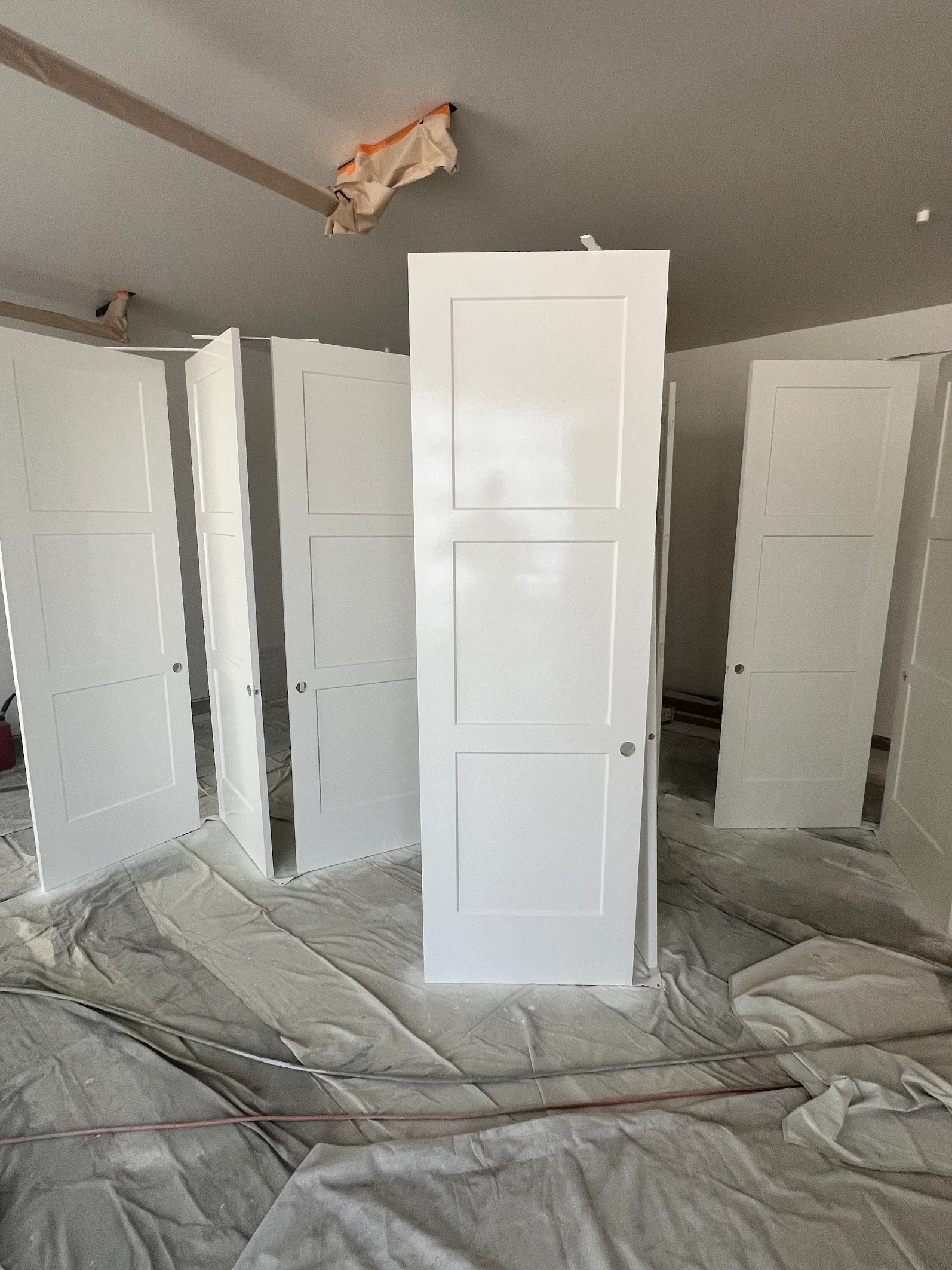 Six-panel white interior doors installed with gray ceiling and walls, drop cloth protection