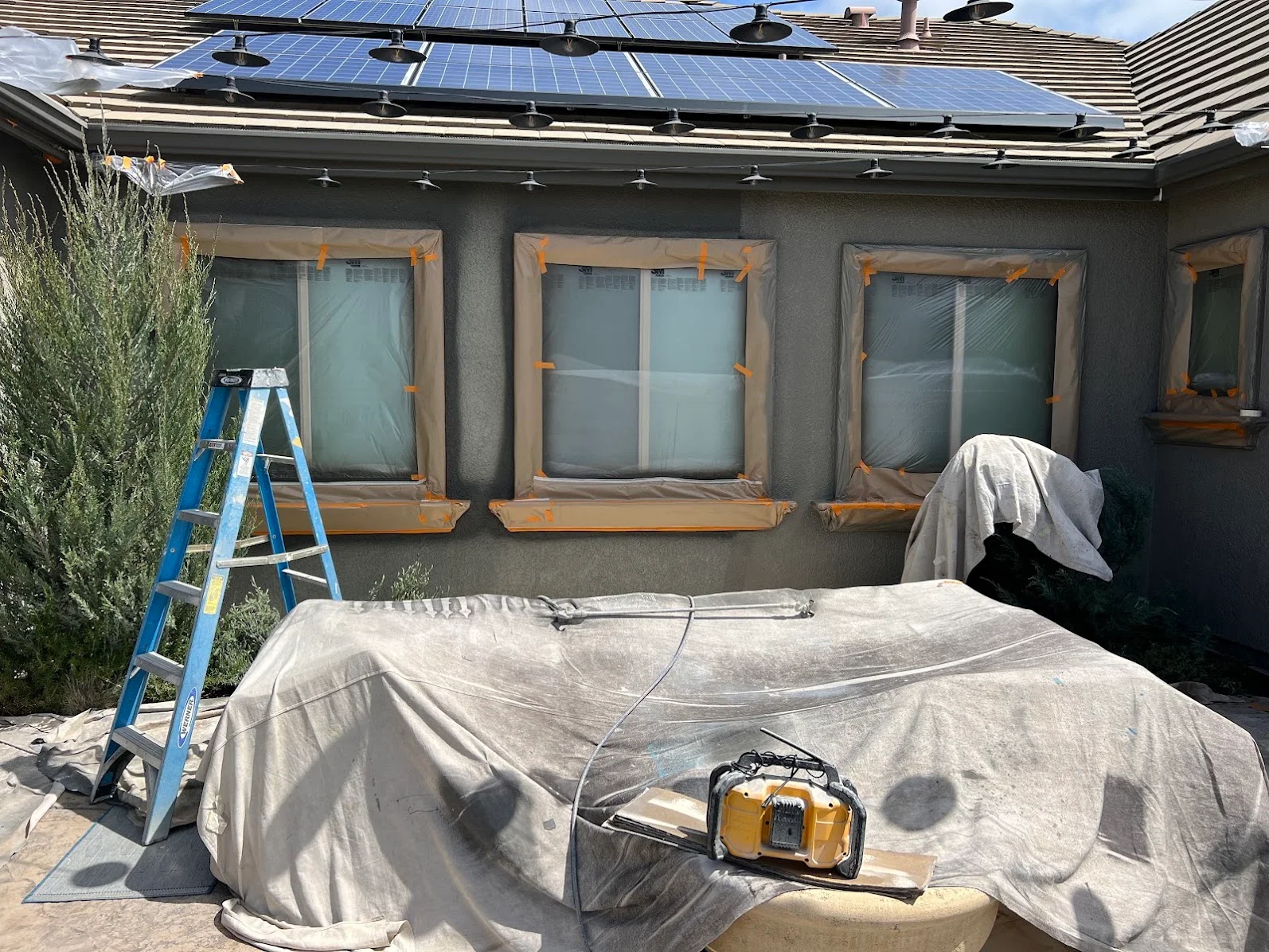 Gray stucco exterior wall with freshly painted finish, protective coverings on windows, solar panels on roof