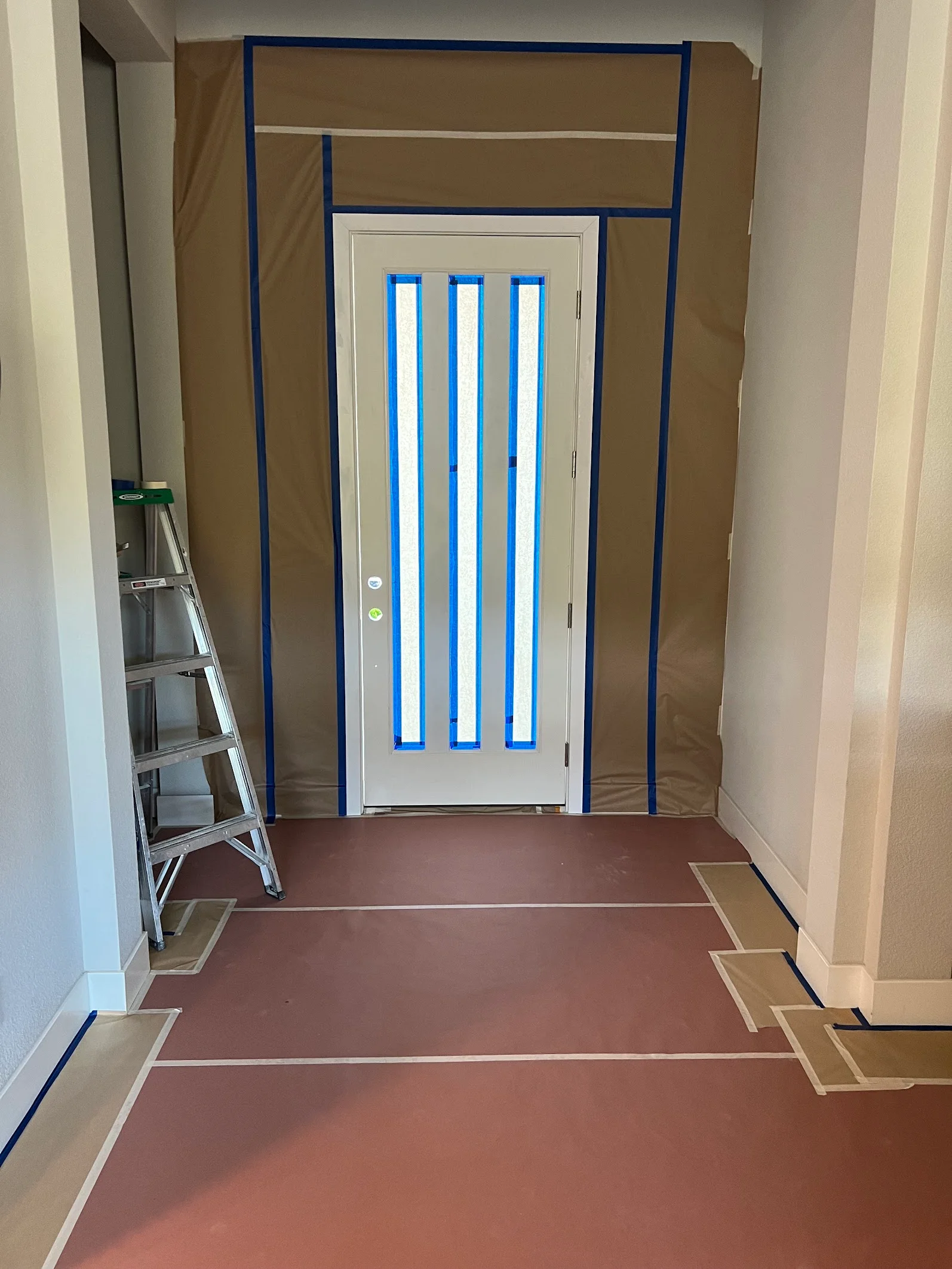 White interior door with three blue glass panels, painted drywall, and protective masking tape during painting project