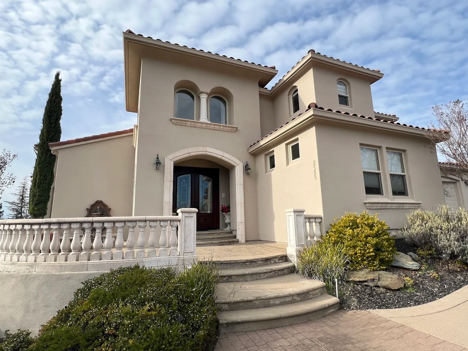 Cream-colored stucco Mediterranean home with arched windows, painted trim, and white balustrade railing