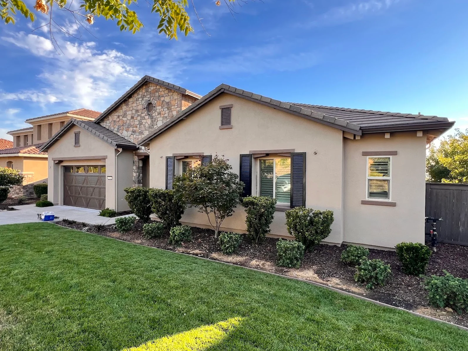 Beige stucco house exterior with dark shutters, stone gable accent, and painted trim