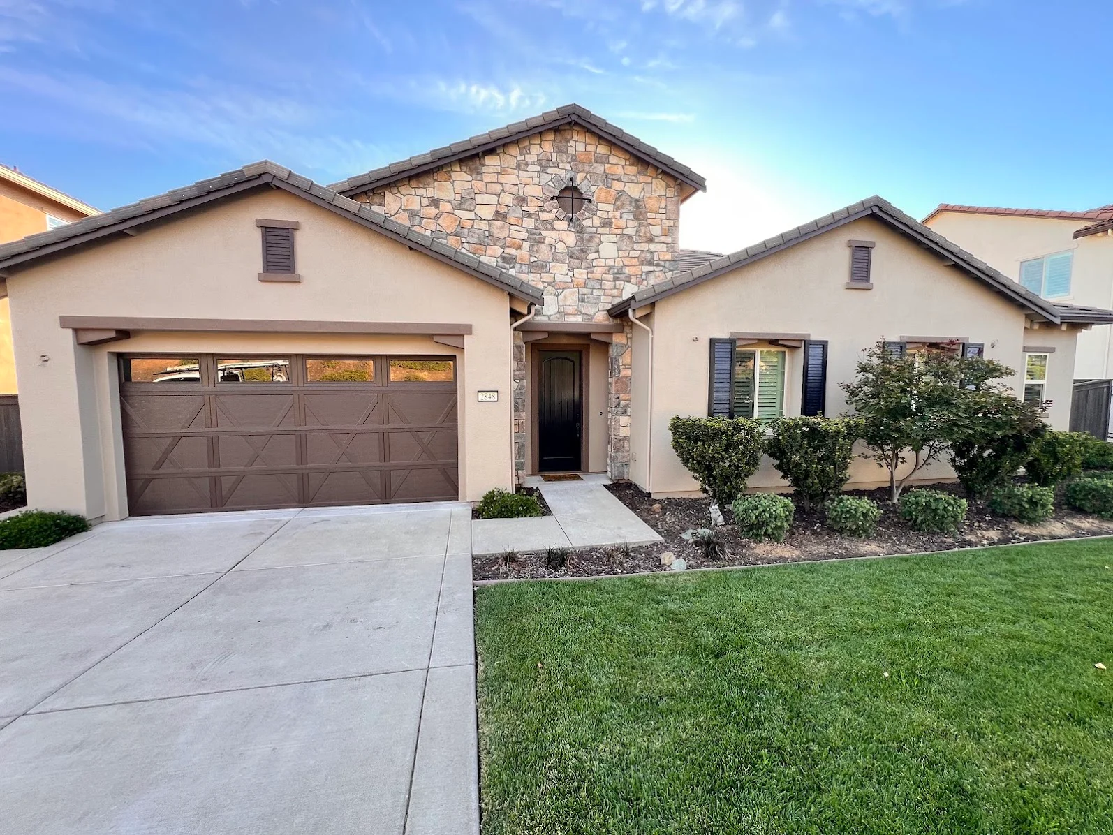 Stucco home with neutral exterior paint, brown garage doors, and stone chimney accent