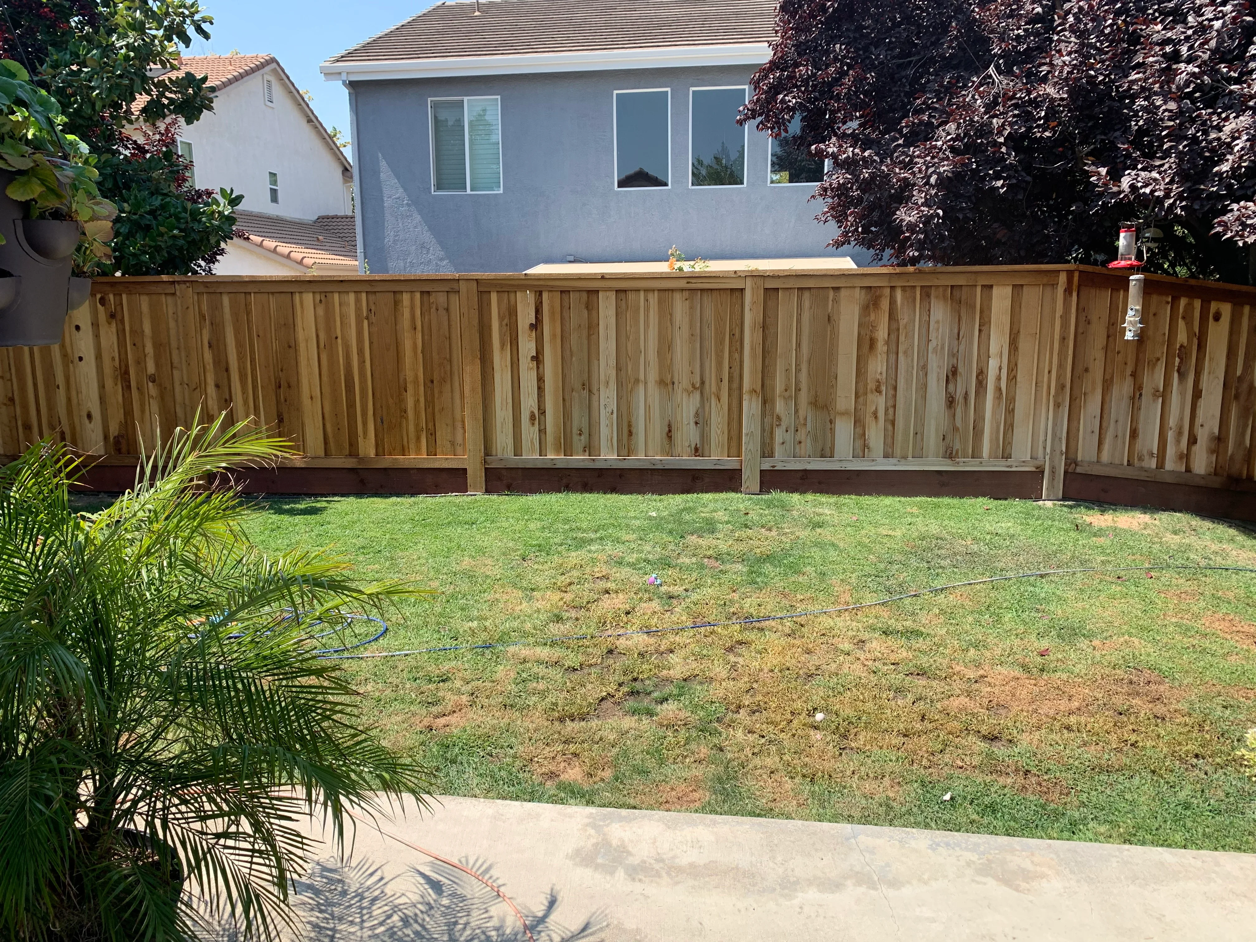 Natural wood-stained privacy fence along residential backyard with mature landscaping