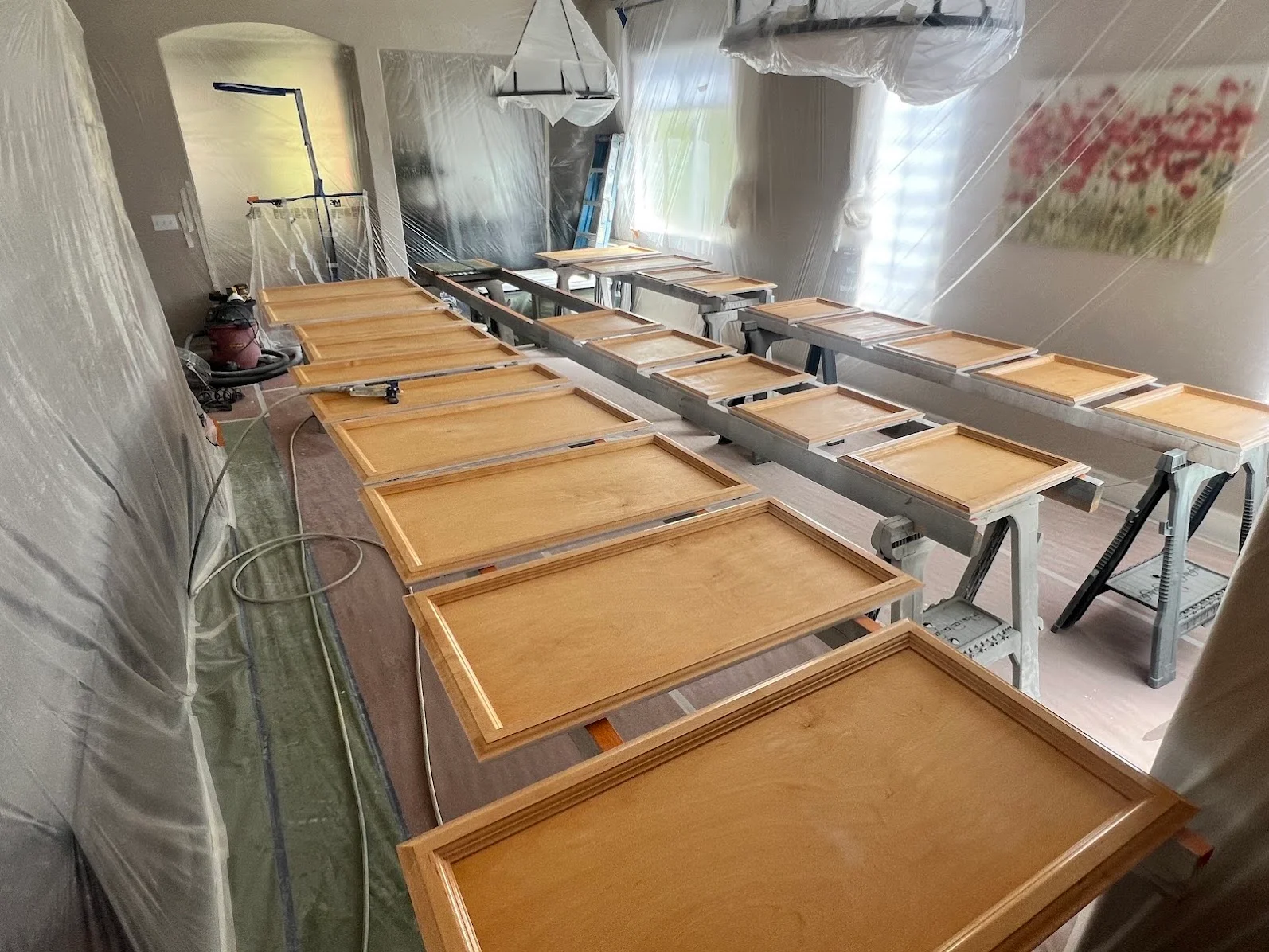 Multiple wood cabinet doors laid out on sawhorses during refinishing process with protective plastic sheeting